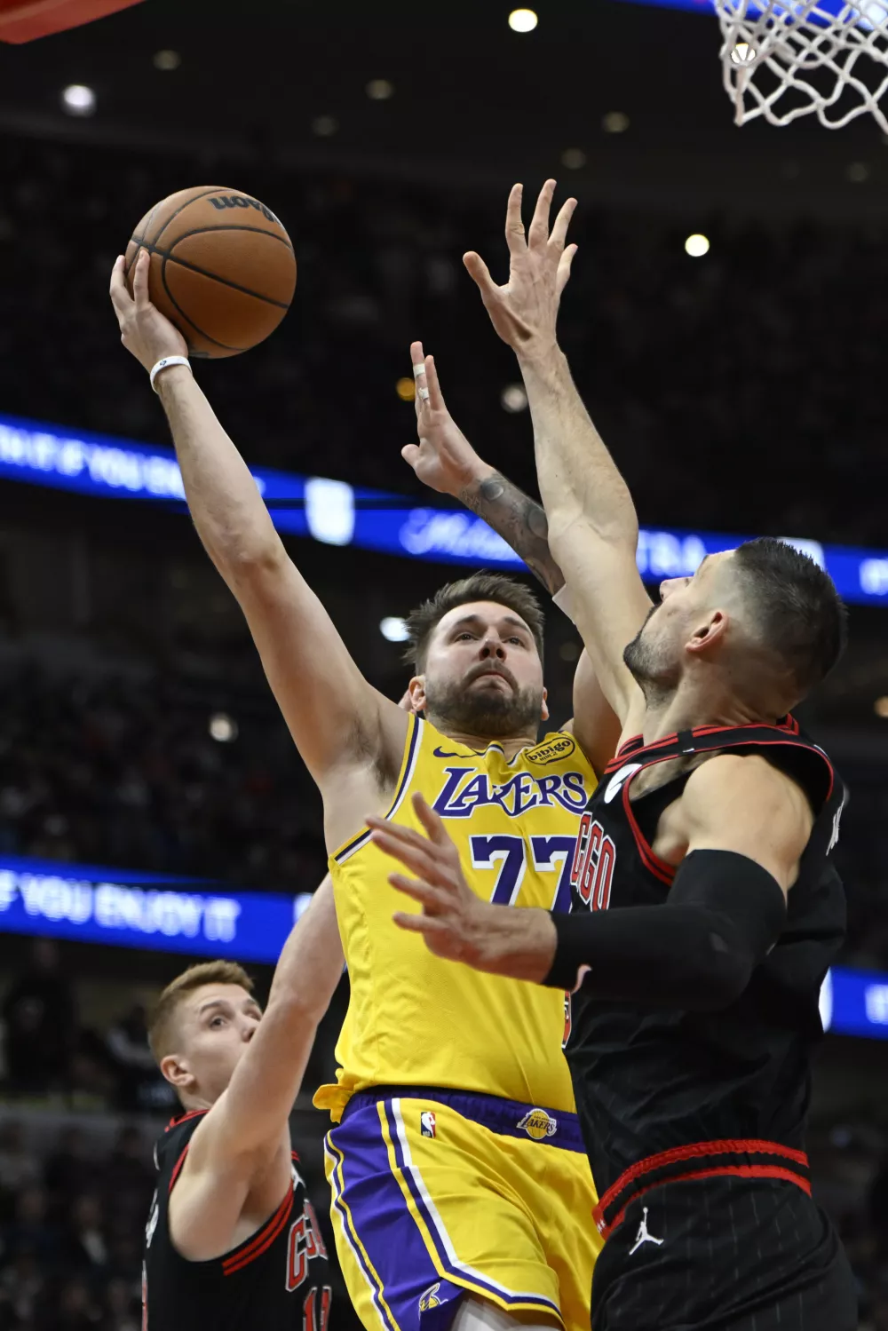 Los Angeles Lakers' Luka Doncic (77) goes up for a shot against Chicago Bulls' Nikola Vucevic (9) and Kevin Huerter (13) during the first half of an NBA basketball game Thursday, March 27, 2025, in Chicago. (AP Photo/Paul Beaty)