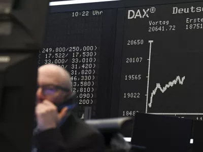 While a stock exchange trader sits in front of his monitors on the trading floor of the Frankfurt Stock Exchange, Germany, the display board with the Dax curve shows a value of less than 20,000 points. (Arne Dedert/dpa via AP)