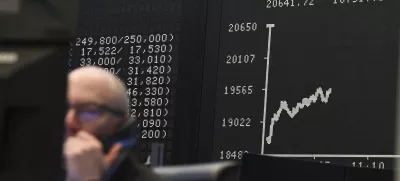 While a stock exchange trader sits in front of his monitors on the trading floor of the Frankfurt Stock Exchange, Germany, the display board with the Dax curve shows a value of less than 20,000 points. (Arne Dedert/dpa via AP)