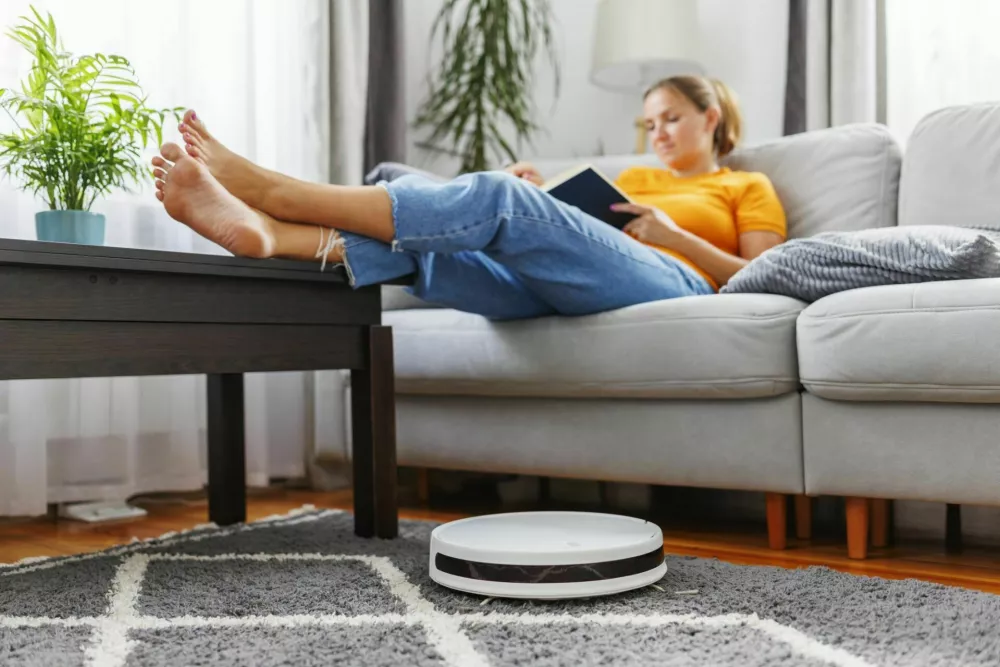 Robotic vacuum cleaner cleaning a room while a woman relaxing, reading book on the sofa. Innovative technologies for cleaning / Foto: Andrii Zorii
