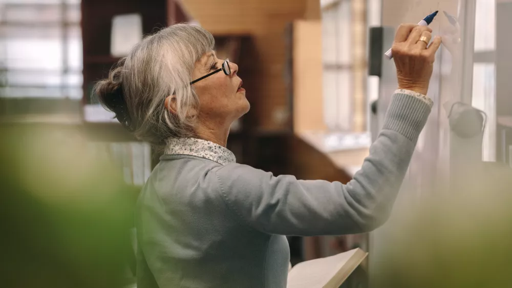 Side view of a senior female teacher writing on a white board in classroom. Close up of a woman lecturer teaching in classroom. / Foto: Jacoblund