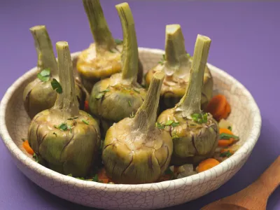 French artichokes &agrave; la Barigoule or Carciofi alla provenzal. Provencal artichokes stewed with carrots, onions, white wine, bay leaves and Proven&ccedil;al herbs. Spring recipes from southern France. Lavender background / Foto: Uliu