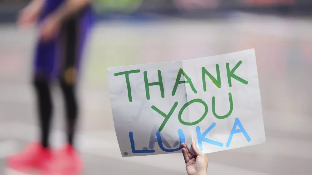 A fan holds up a sign thanking Los Angeles Lakers' Luka Doncic as he stands on the court at rear late in the second half of an NBA basketball game against the Dallas Mavericks in Dallas, Wednesday, April 9, 2025. (AP Photo/LM Otero)