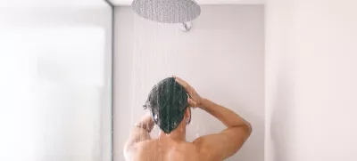 Man taking a shower washing hair with shampoo product under water falling from luxury rain shower head. Morning routine luxury hotel lifestyle guy showering. body care hygiene.