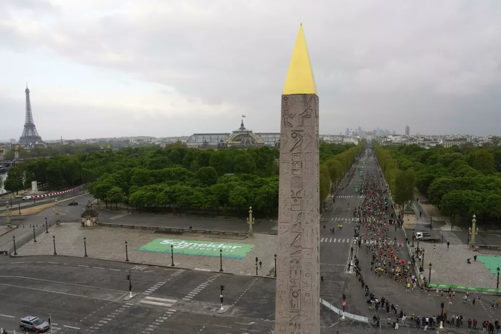 Competitors run on the Champs-Elysees avenue, with the Eiffel Tower, left, and the Obelisk of the Concorde plaza in foreground, during the Paris marathon, in Paris, Sunday, April 13, 2025. (AP Photo/Aurelien Morissard)