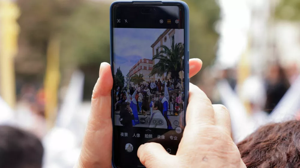 An Asian tourist take a picture with her mobile phone of people acting as 'penitents', belonging to La Pollinica brotherhood as they take part in a Palm Sunday procession at the start of Holy Week, in Ronda, southern Spain April 13, 2025. REUTERS/Jon Nazca