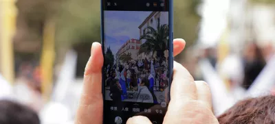 An Asian tourist take a picture with her mobile phone of people acting as 'penitents', belonging to La Pollinica brotherhood as they take part in a Palm Sunday procession at the start of Holy Week, in Ronda, southern Spain April 13, 2025. REUTERS/Jon Nazca