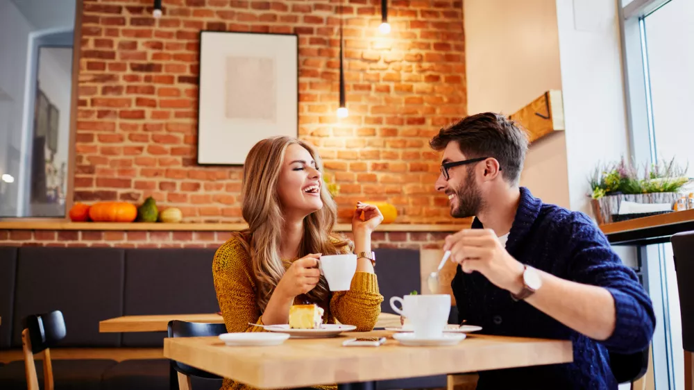Couple of young people drinking coffee and eating cake in a stylish modern cafeteria