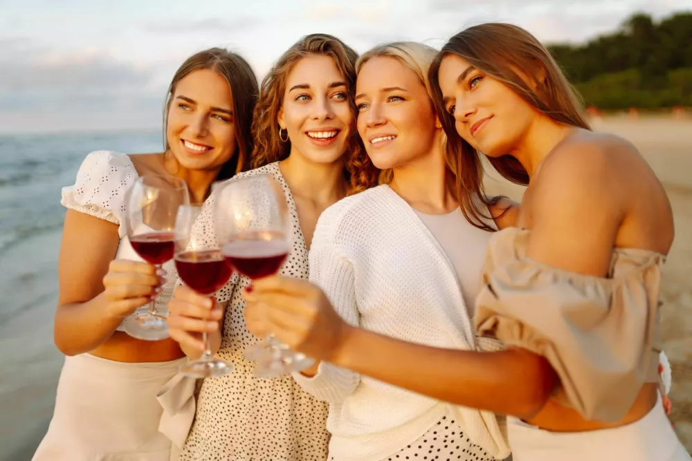 Happy girlfriends on the beach with glasses of wine, enjoying the sunset and nature. Bachelorette. / Foto: Maksym Belchenko