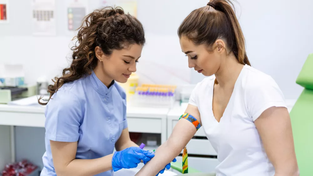 Preparation for blood test with pretty young woman by female doctor medical uniform on the table in white bright room. Nurse pierces the patient's arm vein with needle blank tube. / Foto: Stefanamer