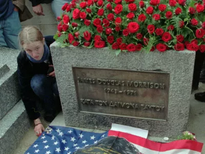A fan of the Doors' lead singer Jim Morrison lays out an American flag with the likeness of the rock poet at his gravesite in Pere Lachaise Cemetery in Paris Wednesday July 3,1996 the day of the 25th anniversary of the rock singer's death. Many fans from Europe, the United States and Japan bearing candles gathered to pay homage to the dead rock star who has gained a cult status. (AP Photo/Michel Lipchitz)
