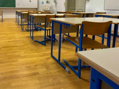 Modern, well-lit classroom with rows of empty wooden desks and blue-framed chairs on a polished wooden floor. The organized, quiet setting evokes themes of education, back to school, academic preparation, and the learning environment. Perfect for content related to schools, teaching, or educational systems.