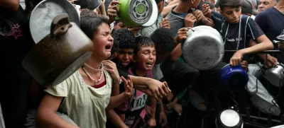 Children react as Palestinians wait to receive food cooked by a charity kitchen, in Beit Lahia, northern Gaza Strip, April 24, 2025. REUTERS/Mahmoud Issa