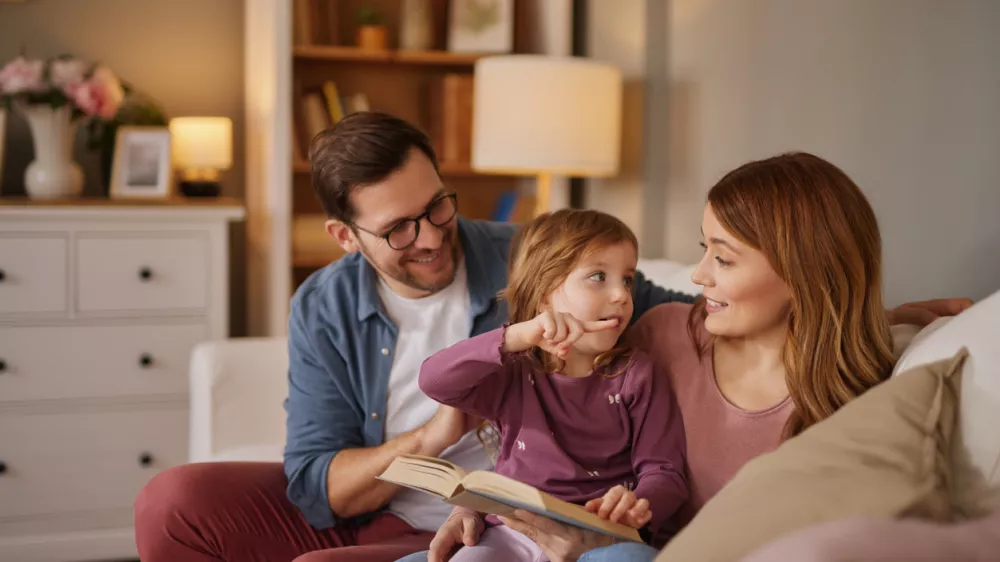 Family with little daughter reading book on sofa in living room