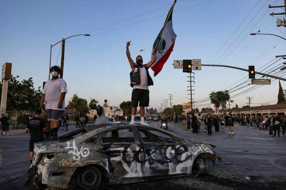 A protester holding a Mexican flag stands on a burnt car during a standoff with law enforcement, following multiple detentions by Immigration and Customs Enforcement (ICE), in the Los Angeles County city of Paramount, California, U.S., June 7, 2025.  REUTERS/Barbara Davidson