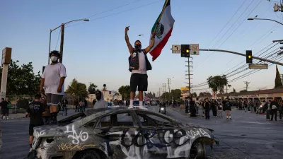 A protester holding a Mexican flag stands on a burnt car during a standoff with law enforcement, following multiple detentions by Immigration and Customs Enforcement (ICE), in the Los Angeles County city of Paramount, California, U.S., June 7, 2025.  REUTERS/Barbara Davidson
