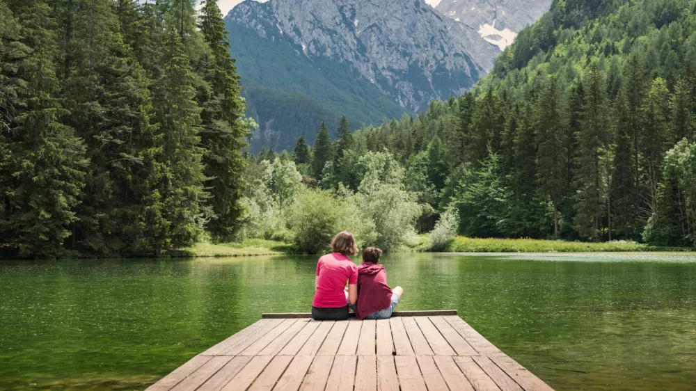 Mother sitting on the dock hugging her son, enjoying the majestic mountain and lake view. Family time and vacation concepts. / Foto: 24k-production