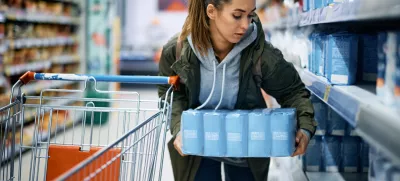Young woman making food supplies and taking large packet of flour while shopping in grocery store.