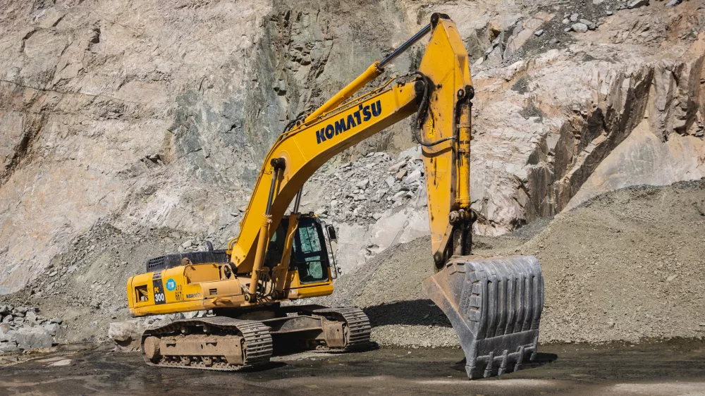 Komatsu PC300 yellow excavator in Almaty mountains, rock formation on the background. Almaty, Kazakhstan - September 28, 2022