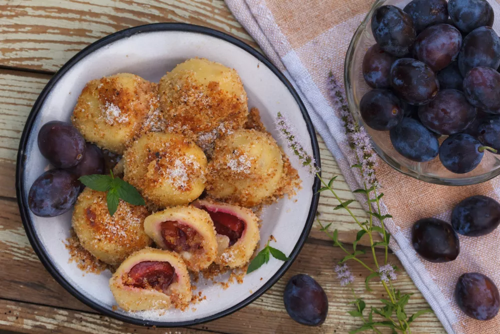 Sweet plum dumplings in metal bowl on wooden table. Homemade dessert with dough and plums. / Foto: Meteo021