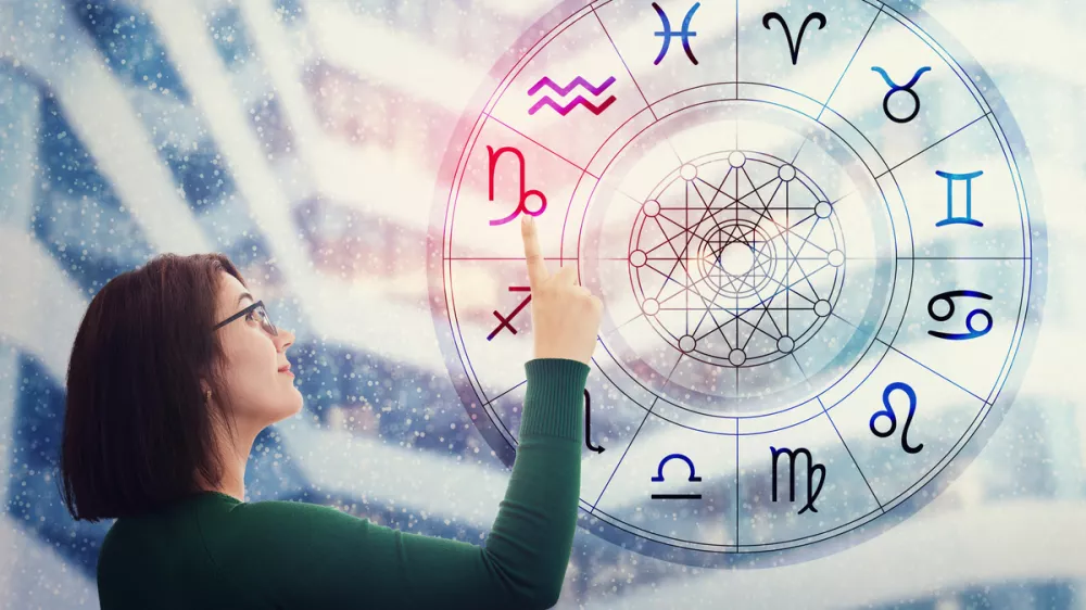 Woman choosing a zodiac sign from the astrological wheel to find the future predictions. Having trust in horoscope, consulting stars and believe in the power of universe. Astrology esoteric concept. / Foto: Bulat Silvia