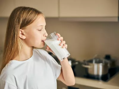 Side view of a blonde Caucasian teen taking a sip of milk from the glass / Foto: Yacobchuk