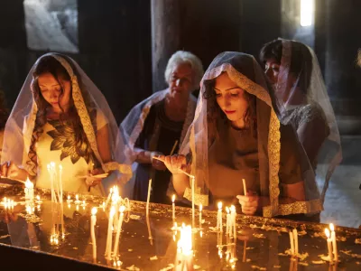 August 18, 2018. Armenia, Ararat Province. Geghard Monastery interior. Young women in headscarfs or shawls lighting candles.