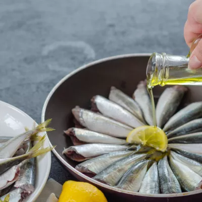 Woman is pouring olive oil into the pan. / Foto: Nkeskin