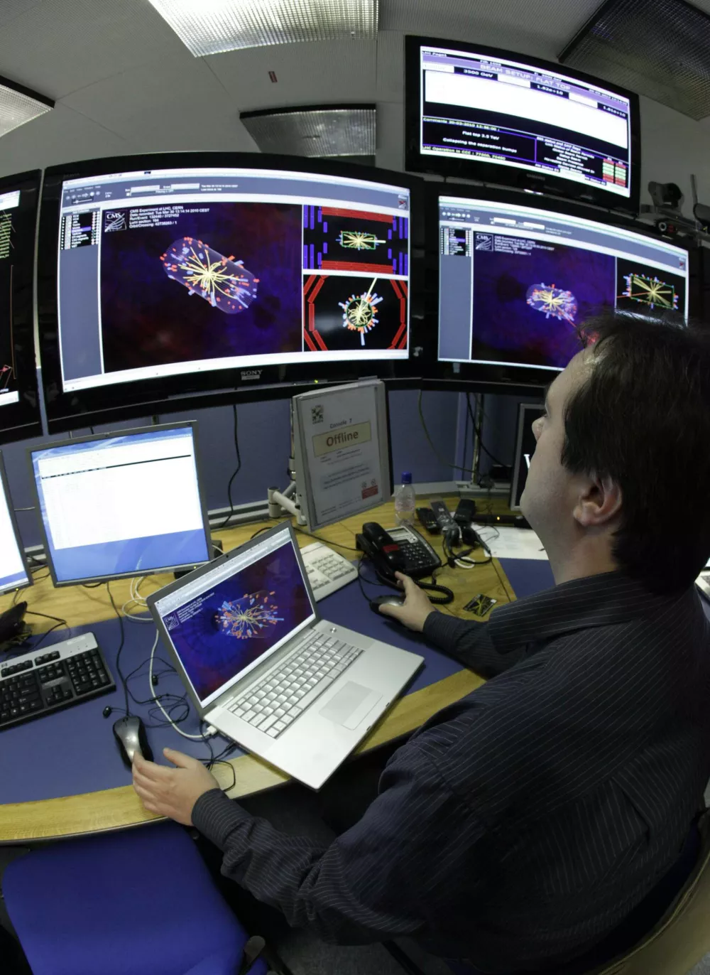 A scientist looks at pictures of the first successful collisions at full power at the Compact Muon Solenoid (CMS) experience control room of the Large Hadron Collider (LHC) at the European Organisation for Nuclear Research (CERN) in Meyrin, near Geneva March 30, 2010. Scientists at the CERN research centre will begin trying on Tuesday to make particles collide at ultra-high power and close to the speed of light to create mini-versions of the "Big Bang" that gave birth to the universe. Picture taken with a fisheye lense.  REUTERS/Denis Balibouse (SWITZERLAND - Tags: SCI TECH SOCIETY)