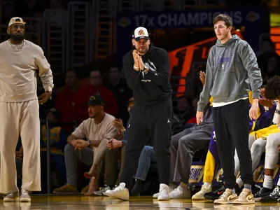 Mar 20, 2025; Los Angeles, California, USA; Los Angeles Lakers forward LeBron James (23), guard Luka Doncic (77), and guard Austin Reaves (15) on the sidelines against the Milwaukee Bucks during the first half at Crypto.com Arena. Mandatory Credit: Jonathan Hui-Imagn Images