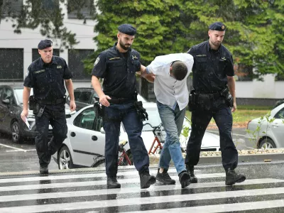 Emanuel Rep v spremstvu policistov na zasli&scaron;anje v Varaždinu. Sumijo ga umora mame s sekiro ter poskusa umorov polbrata in očima. 