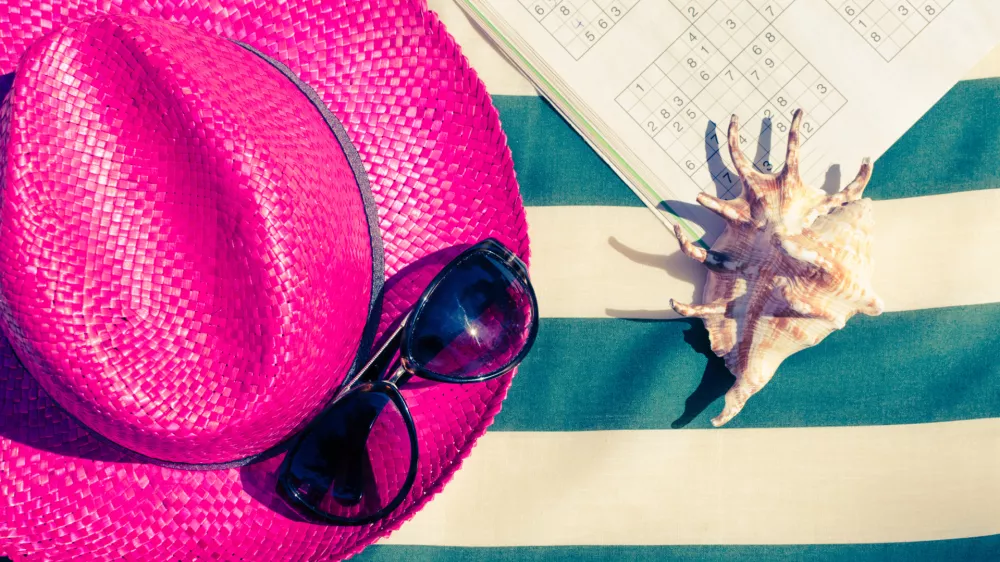 Colorful holiday background with pink straw beach hat with sunglasses and sudoku on striped sunbed. Summer vacation beach leisure activity under the sunlight concept. Flat lay. Top view. Copy space. / Foto: Nellisyr