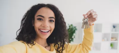 Selfie photo of smiling american happy young girl own her first apartment holding keys relocate to new house indoors loft living room. / Foto: Deagreez