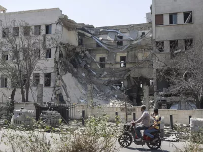 People pass in front the Syrian Defense Ministry building which on Wednesday was heavily damaged by Israeli airstrikes in Damascus, Syria, Thursday, July 17, 2025. (AP Photo/Ghaith Alsayed)