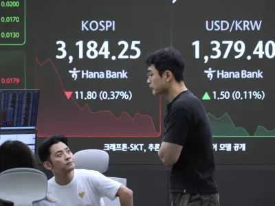 Currency traders work near a screen showing the Korea Composite Stock Price Index (KOSPI) and the foreign exchange rate between U.S. dollar and South Korean won, right, at the foreign exchange dealing room of the Hana Bank headquarters in Seoul, South Korea, Monday, July 28, 2025. (AP Photo/Ahn Young-joon)