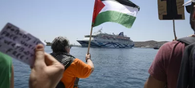 A protester waves a Palestinian flag as people demonstrates in front of a cruise ship carrying Israeli tourists and trying to approach the Aegean Sea island of Syros, Greece, Tuesday, July 22, 2025. (Nikos Panagiotopoulos/InTime News via AP)