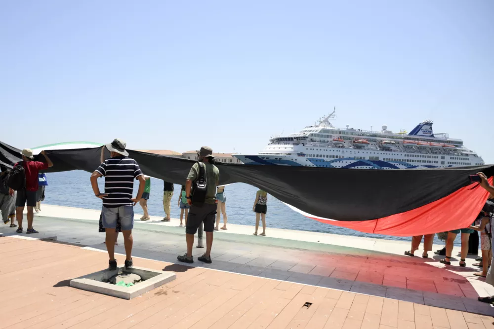 Protesters hold a Palestinian flag demonstrating as a cruise ship carrying Israeli tourists try to approach the Aegean Sea island of Syros, Greece, Tuesday, July 22, 2025. (Nikos Panagiotopoulos/InTime News via AP)