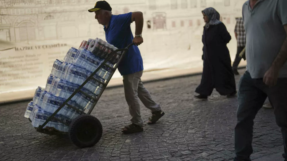 A man delivers plastic bottles of water to a local restaurant on a hot summer day at Eminonu district, in Istanbul, Turkey, Friday, July 25, 2025. (AP Photo/Francisco Seco)