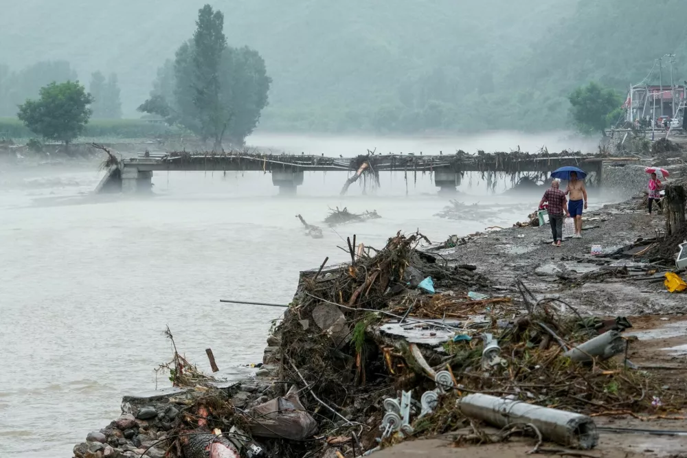 People walk by a damaged bridge after heavy rainfall flooded the area, in Huairou district of Beijing, China July 28, 2025. cnsphoto via REUTERS  ATTENTION EDITORS - THIS IMAGE WAS PROVIDED BY A THIRD PARTY. CHINA OUT. NO COMMERCIAL OR EDITORIAL SALES IN CHINA