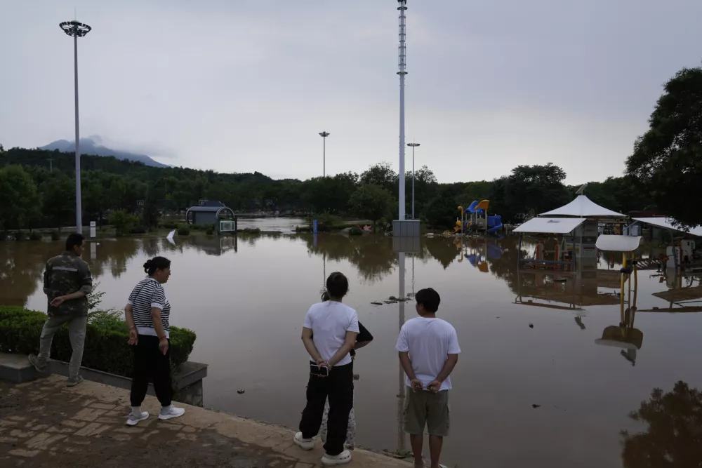 People looking at a park filled with flooded water after heavy rains in Miyun district on the outskirts of Beijing, China, Monday, July 28, 2025. (AP Photo/Mahesh Kumar A.)