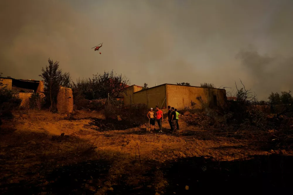 A firefighting helicopter flies over as local residents stand near burned areas after a wildfire in Congosta, Spain, August 11, 2025. REUTERS/Susana Vera