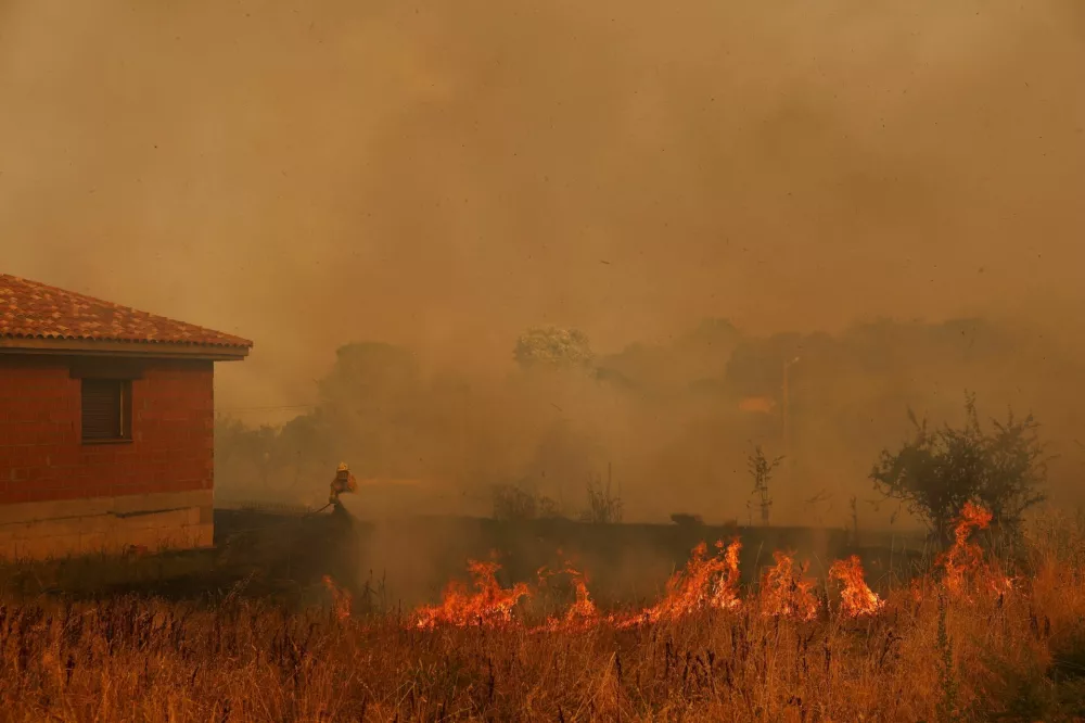 A firefighter battles a wildfire by a house in Congosta, Spain, August 11, 2025. REUTERS/Susana Vera