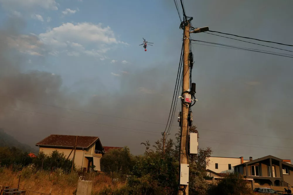 A firefighting helicopter flies over Rogami suburbs while smoke rises, as temperature rises during a heatwave in Podgorica, Montenegro, August 11, 2025. REUTERS/Stevo Vasiljevic