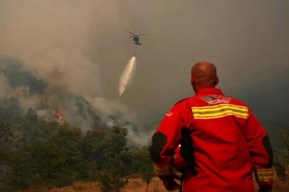 A member of emergency services watches as a firefighting helicopter works to contain a wildfire near Finiq, Albania, August 11, 2025. REUTERS/Florion Goga