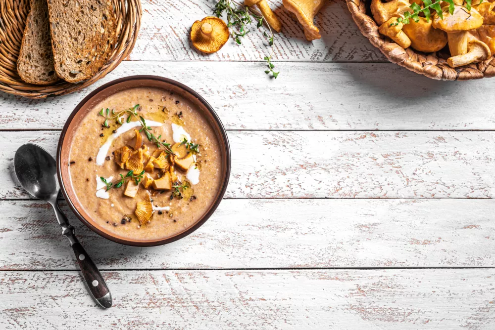Chanterelle mushroom soup with thyme and fresh mushrooms on white wooden background, top view, copy space. Bowl of autumn seasonal cream soup with forest chanterelles. / Foto: Mizina