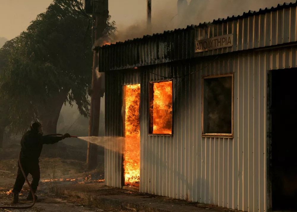 A firefighter works to extinguish a fire from a building during a wildfire, in Sichaina near Patras, Greece, August 13, 2025. REUTERS/Louiza Vradi   TPX IMAGES OF THE DAY