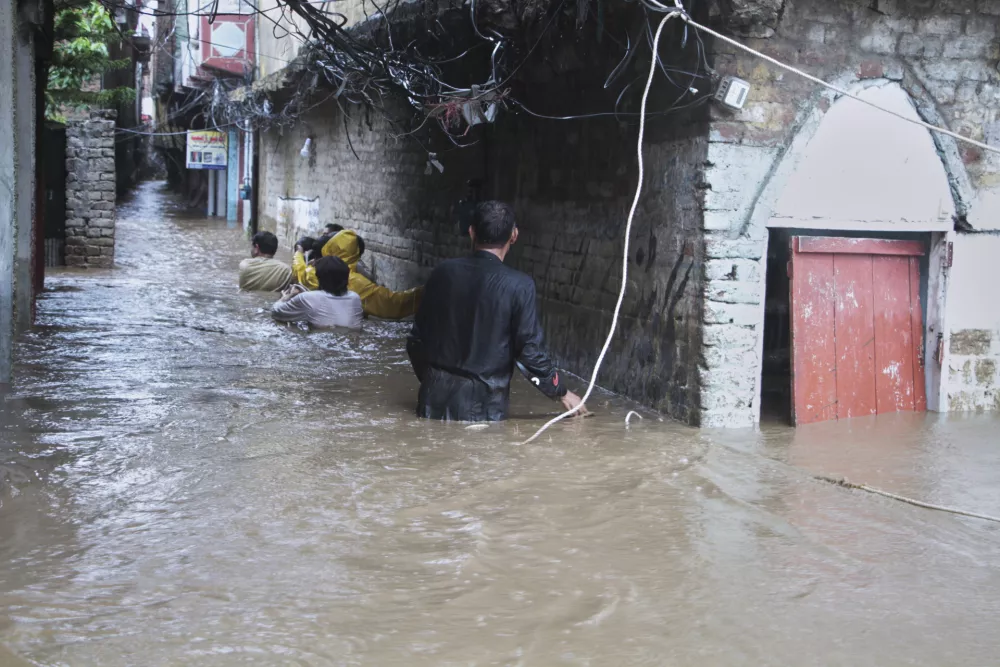 Local residents navigate through a flooded street following flash flooding due to heavy rains at a neighbourhood of Mingora, the main town of Swat Valley, northwestern Pakistan, Friday, Aug. 15, 2025. (AP Photo/Naveed Ali)