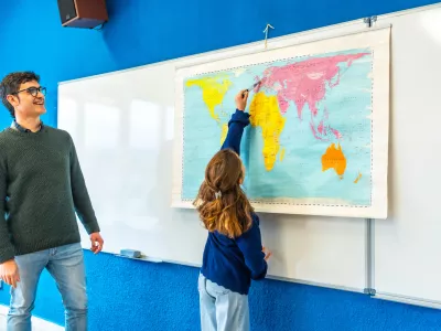 Girl pointing at world map during geography lesson with her teacher in elementary school classroom / Foto: Unaihuiziphotography