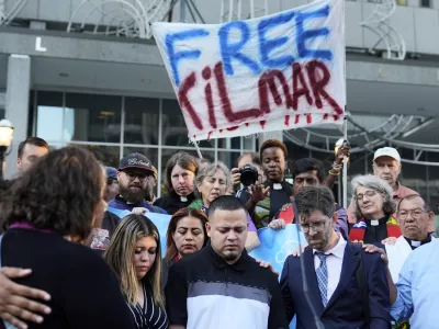 Jennifer Vasquez Sura, front left, her husband Kilmar Abrego Garcia, front center, and Attorney Simon Sandoval-Moshenberg, front right, attend a protest rally at the Immigration and Customs Enforcement field office in Baltimore, Monday, Aug. 25, 2025, to support Kilmar Abrego Garcia. (AP Photo/Stephanie Scarbrough)