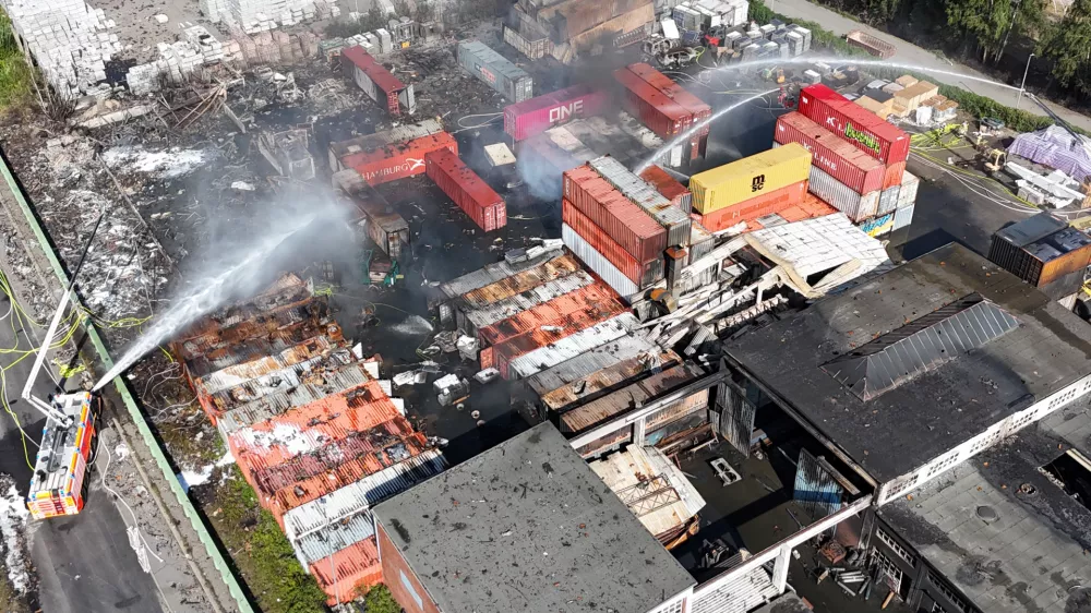 26 August 2025, Hamburg: Aerial view of firefighters extinguishing a fire in an industrial area in the port of Hamburg, where a major fire had broken out the day before. Photo: Marcus Golejewski/dpa